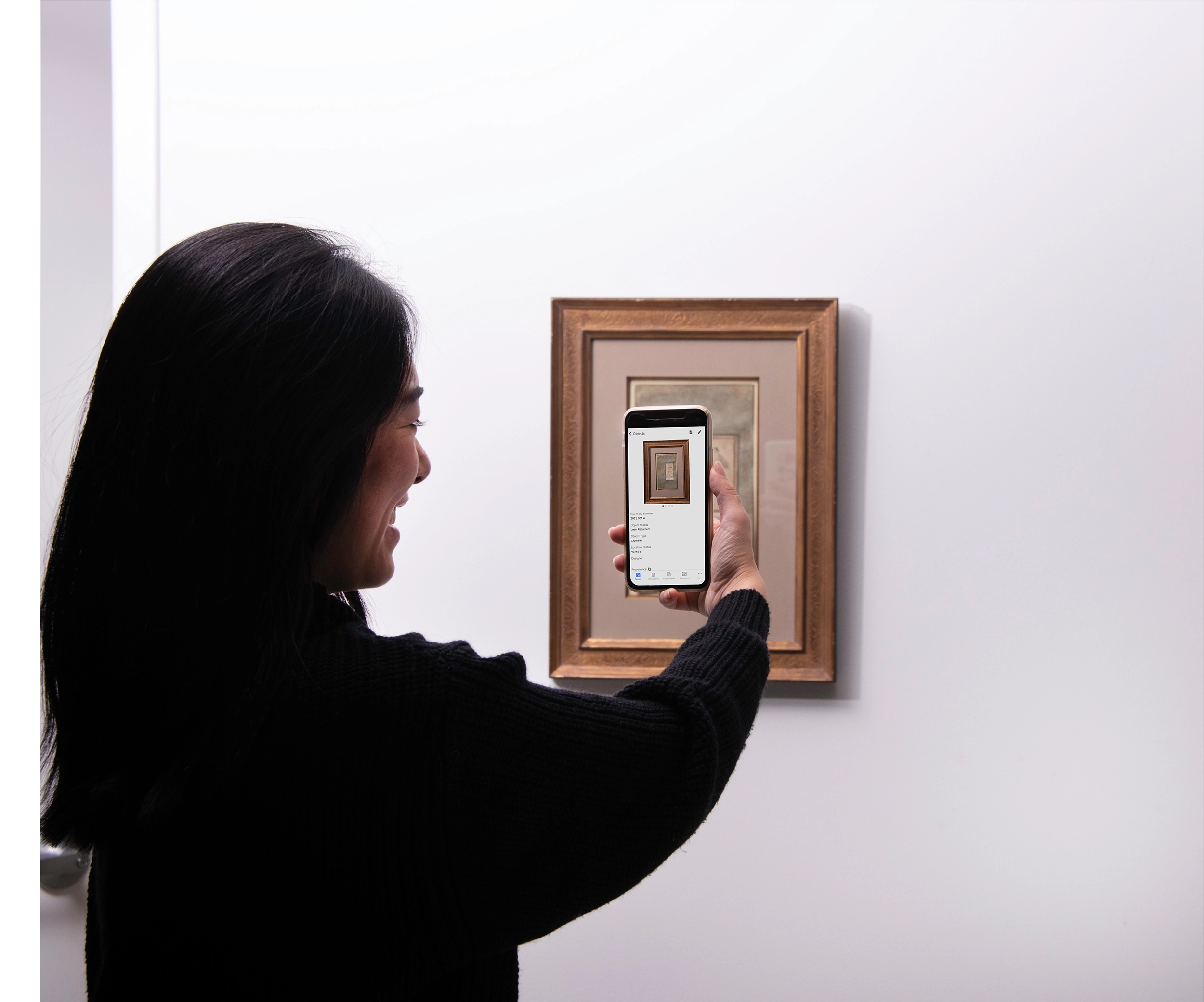 Woman holding iPhone in front a piece of art